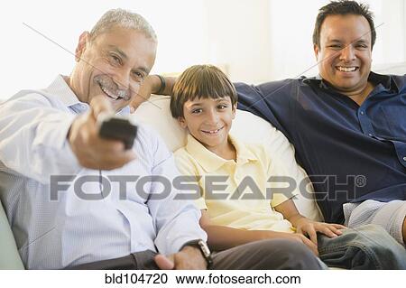 Stock Image - Hispanic grandfather, father and son watching television. Fotosearch