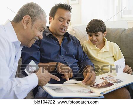 Stock Image - Hispanic grandfather, father and son looking at photo album. Fotosearch