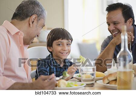 Stock Image - Hispanic grandfather, father and son eating dinner. Fotosearch