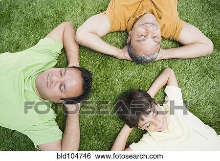 Stock Photograph - Hispanic grandfather, father and son laying in grass. Fotosearch
