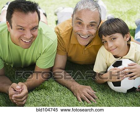 Stock Photography - Hispanic grandfather, father and son laying in grass. Fotosearch