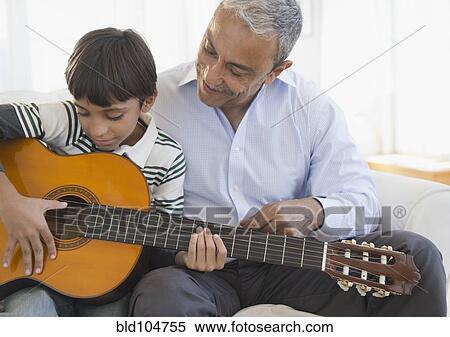 Stock Photography - Hispanic grandfather watching grandson playing guitar. Fotosearch