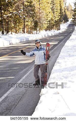 Stock Photography - Hispanic man with skis hitchhiking. Fotosearch