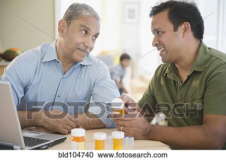 Stock Image - Hispanic son explaining medication to father. Fotosearch