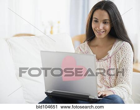 Stock Image - Hispanic teenager using laptop in bedroom. Fotosearch