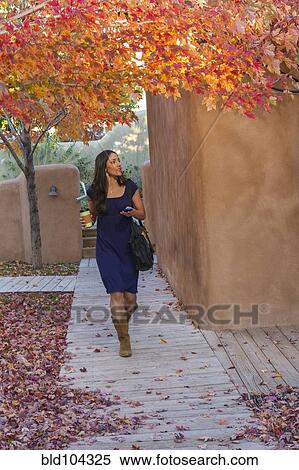 Stock Photography - Hispanic woman carrying coffee and text messaging on cell phone. Fotosearch