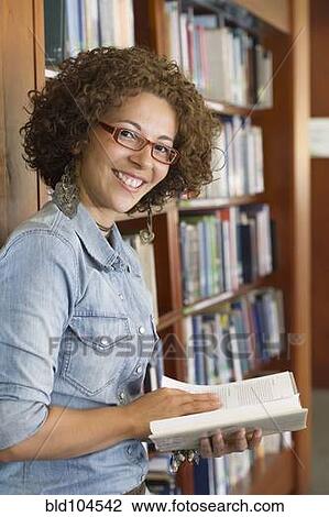 Stock Image - Hispanic woman reading book in library. Fotosearch