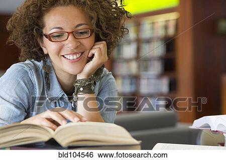 Stock Photograph - Hispanic woman reading book in library. Fotosearch
