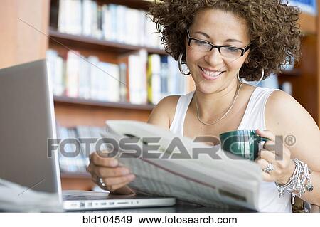 Stock Photo - Hispanic woman reading newspaper in library. Fotosearch