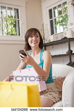 Stock Photograph - Hispanic woman sitting with shopping bags and cell phone. Fotosearch