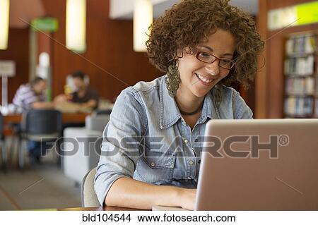 Picture - Hispanic woman using laptop in library. Fotosearch