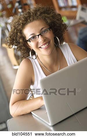Stock Image - Hispanic woman using laptop in library. Fotosearch
