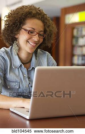 Stock Photography - Hispanic woman using laptop in library. Fotosearch