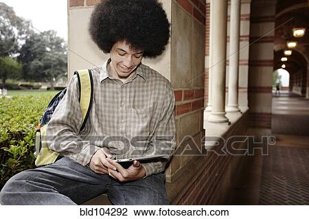 Stock Image - Man with afro using digital tablet outdoors. Fotosearch