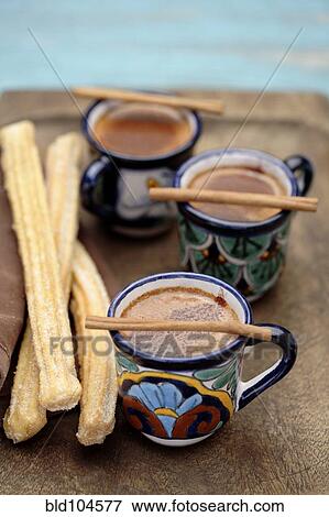 Stock Photo - Mexican hot chocolate with cinnamon sticks and churros. Fotosearch