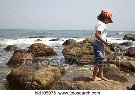 Stock Photography - Mixed race boy standing on rocks near ocean. Fotosearch
