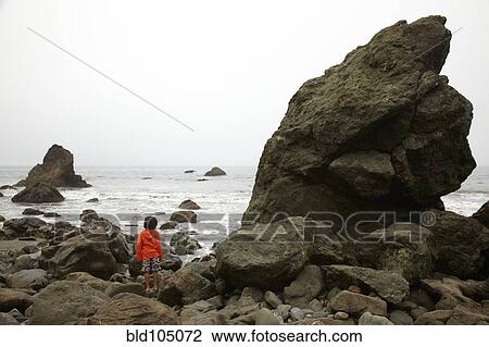 Stock Image - Mixed race climbing on rocks near ocean. Fotosearch