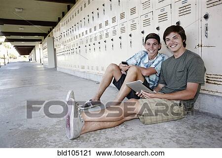 Stock Image - School friends leaning on lockers using digital tablet. Fotosearch