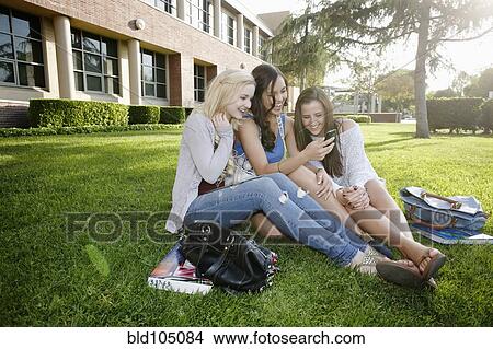 School friends sitting in grass looking at cell phone View Large Photo Image Picture - School friends sitting in grass looking at cell phone. Fotosearch