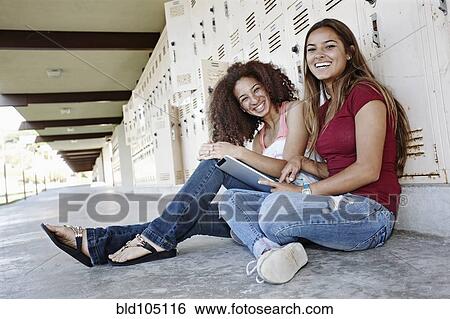 Stock Photograph - School friends sitting near lockers with digital tablet. Fotosearch