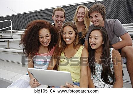Picture - School friends sitting together on bleachers using digital tablet. Fotosearch