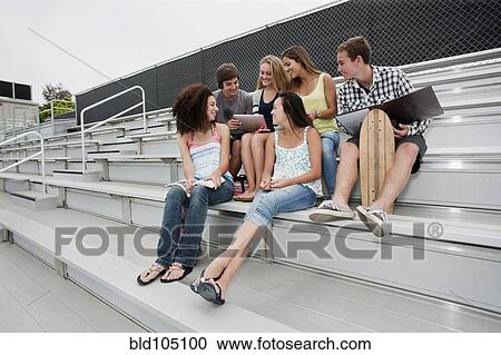 Stock Image - School friends sitting together on bleachers. Fotosearch