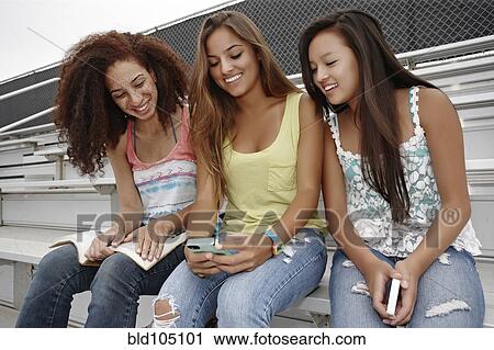 School friends sitting together on bleachers looking at cell phone View Large Photo Image Stock Image - School friends sitting together on bleachers looking at cell phone. Fotosearch