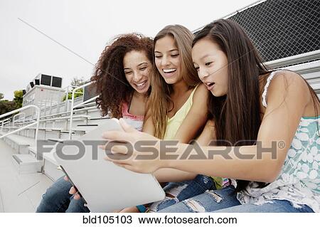 Stock Image - School friends sitting together on bleachers using digital tablet. Fotosearch