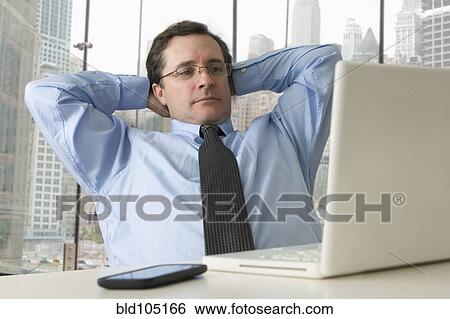 Stock Photograph - Serious Caucasian businessman with hands behind head. Fotosearch