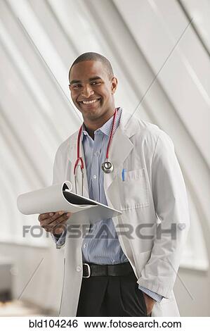 Stock Photograph - Smiling Black doctor standing with hands in pockets. Fotosearch