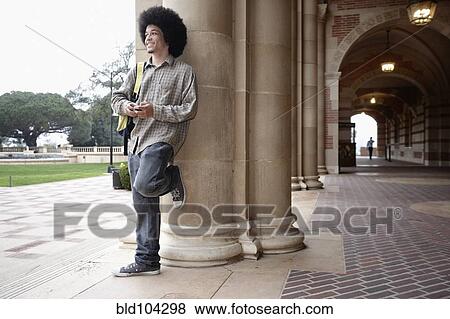 Stock Photo - Student with afro leaning against pillar on campus. Fotosearch