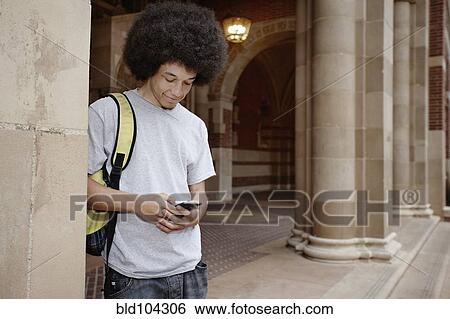 Stock Photograph - Student with afro text messaging on cell phone. Fotosearch