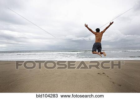 Stock Image - Young man jumping for joy on beach. Fotosearch