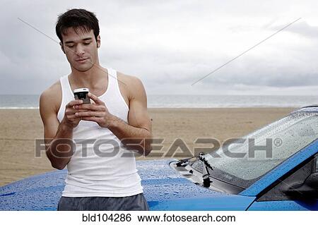 Young man leaning on sports car holding cell phone View Large Photo Image Stock Photograph - Young man leaning on sports car holding cell phone. Fotosearch