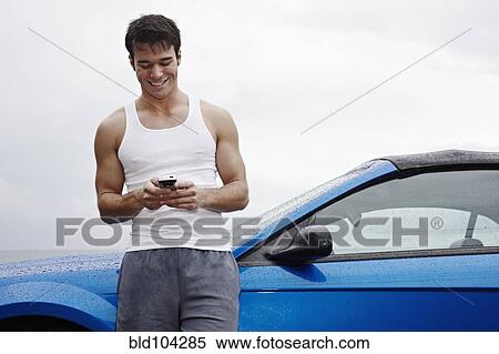 Stock Photography - Young man leaning on sports car holding cell phone. Fotosearch