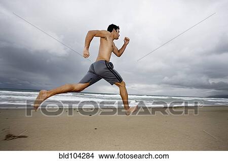 Picture - Young man running on beach. Fotosearch
