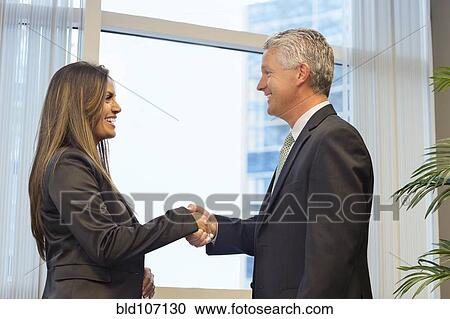 Stock Image - Business people shaking hands in office. Fotosearch