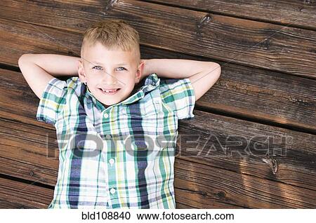 Stock Image - Caucasian boy laying on wooden deck. Fotosearch