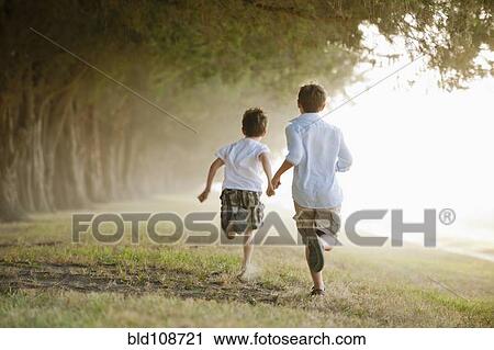 Stock Image - Caucasian boys running in orchard. Fotosearch