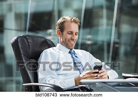 Stock Image - Caucasian businessman using cell phone at desk. Fotosearch