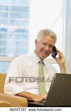 Stock Photo - Caucasian businessman using laptop and cell phone. Fotosearch
