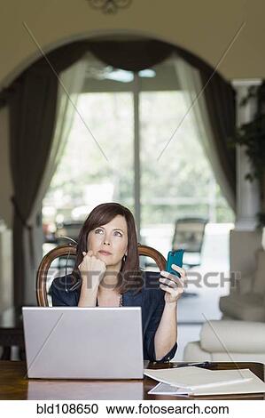 Stock Image - Caucasian businesswoman holding cell phone and looking up. Fotosearch