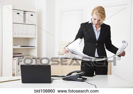 Stock Image - Caucasian businesswoman reading blueprints in office. Fotosearch
