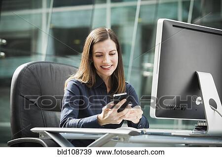 Stock Photo - Caucasian businesswoman using cell phone at desk. Fotosearch
