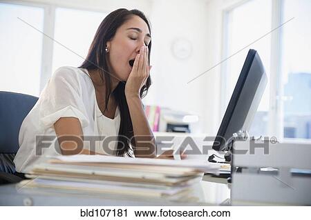 Stock Image - Caucasian businesswoman yawning at desk. Fotosearch