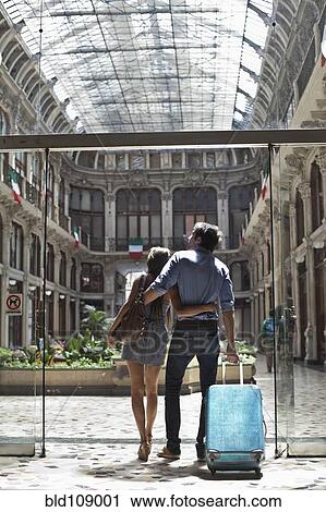 Stock Image - Caucasian couple pulling luggage into ornate building. Fotosearch