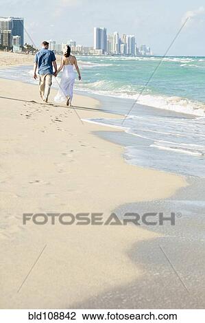 Stock Image - Caucasian couple walking on beach. Fotosearch