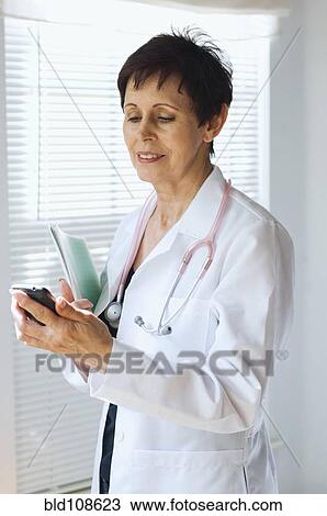 Stock Image - Caucasian doctor using cell phone in office. Fotosearch