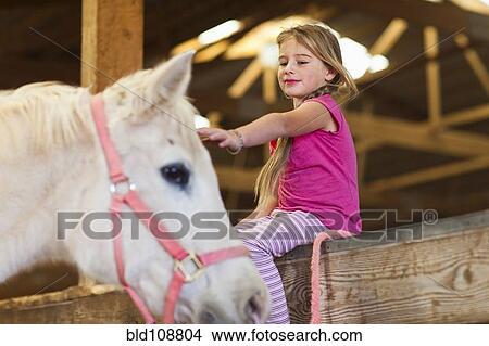 Picture - Caucasian girl petting horse in barn. Fotosearch