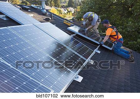 Stock Image - Caucasian men installing panels on roof. Fotosearch